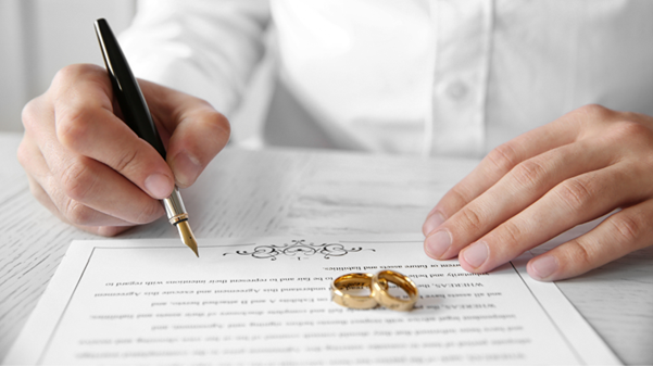 Eine Person mit einem Stift, die auf einer Heiratsurkunde unterschreibt 